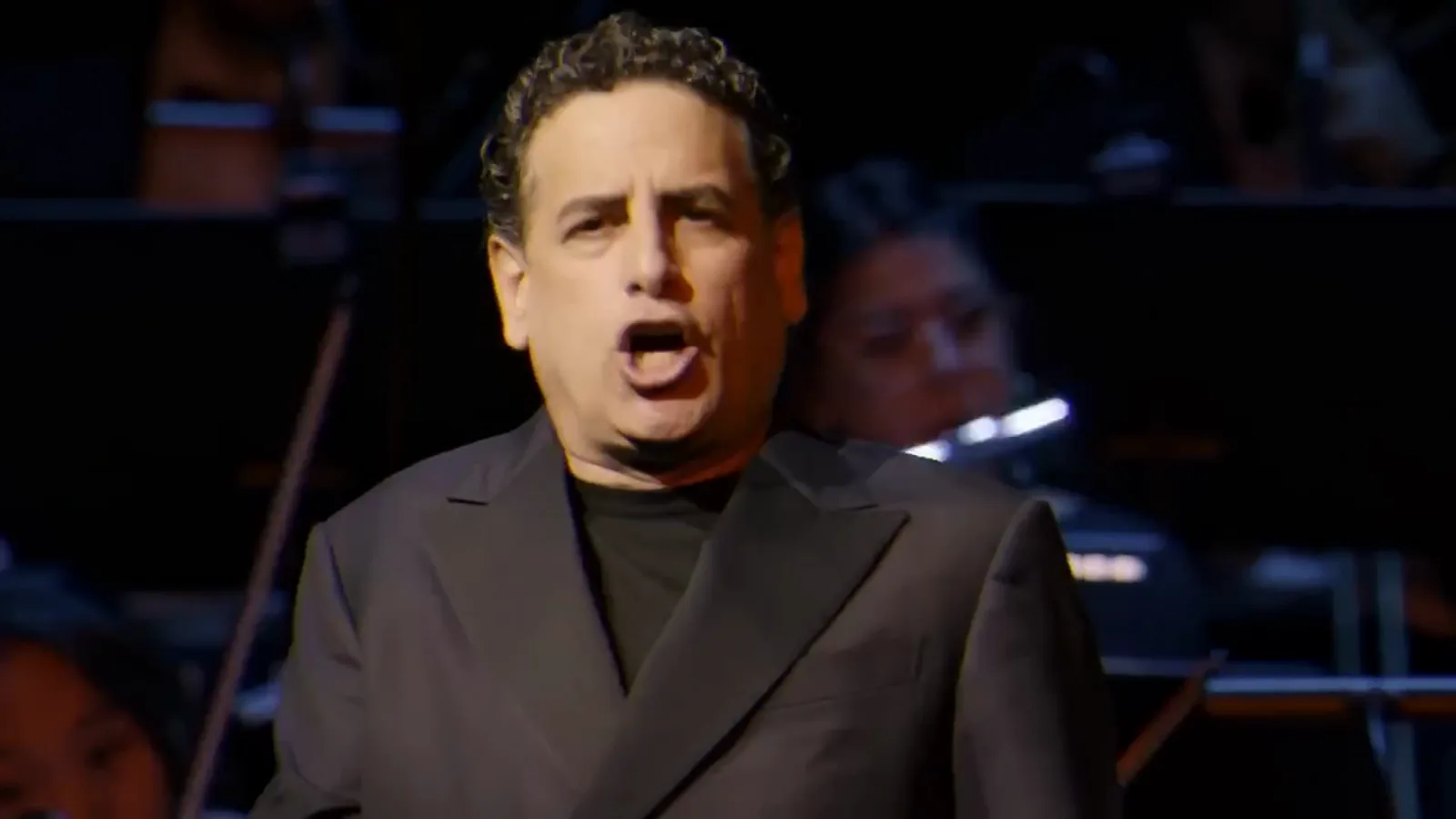 Un cantante interpretando un aria en el escenario, con la orquesta detrás