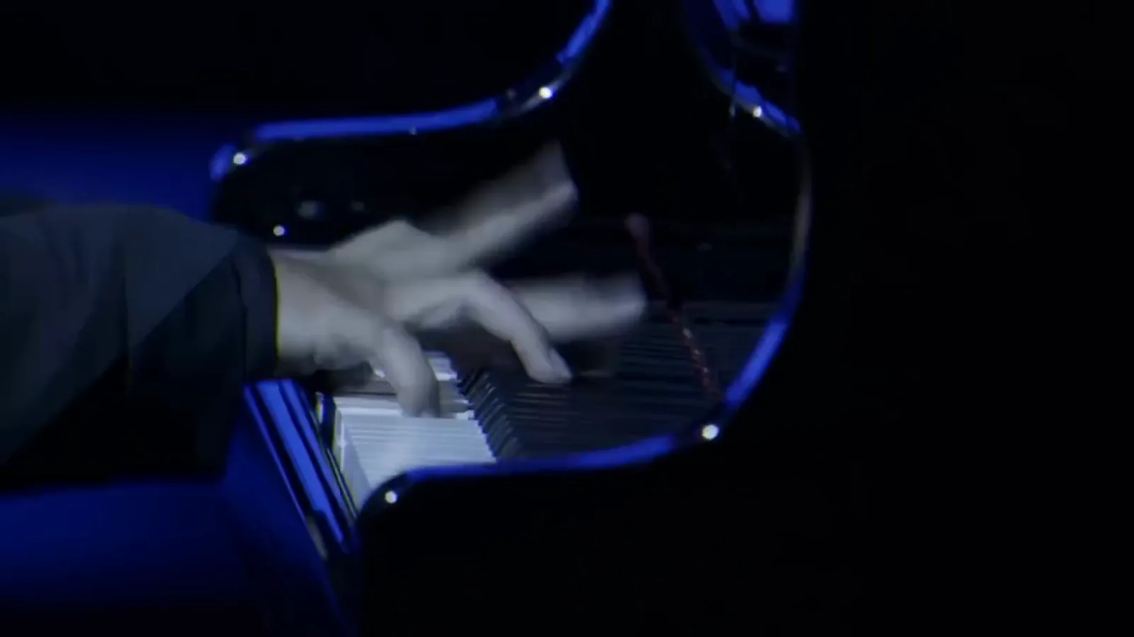Manos de un pianista tocando un piano de cola bajo luz azul